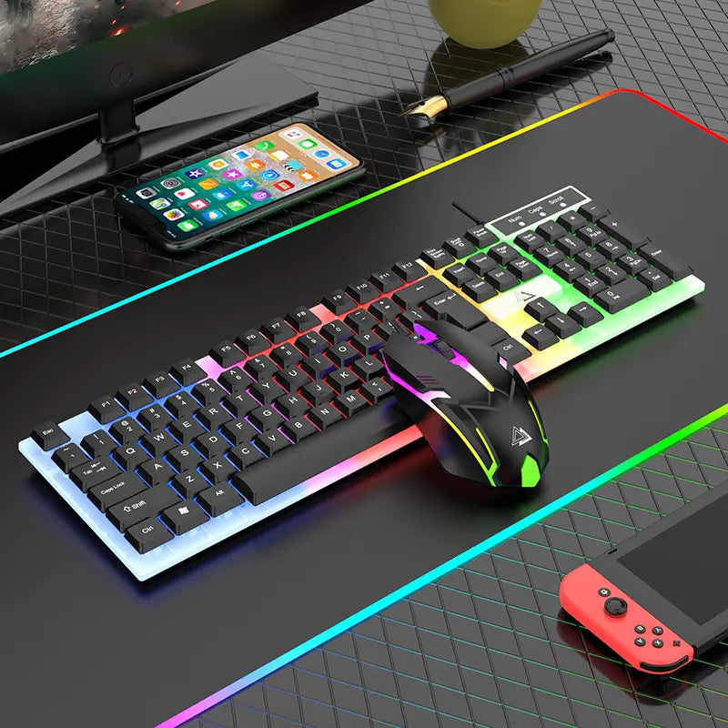 A modern, RGB illuminated Clevisco mechanical gaming keyboard and Clevisco gaming mouse on a desk, surrounded by a smartphone, a game controller, and a monitor. The keyboard emits RGB light from under the keys and the mouse has RGB lights. To the left of the keyboard, there’s a smartphone displaying numerous app icons. On the right side, part of a red game controller is visible. The keyboard and mouse are placed on the Clevisco RGB gaming mousepad.
